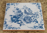 Vintage-style kitchen trivet on ceramic tile. Painting with 2 birds and flowers in blue colors. Retro-style kitchen decor in blue colors.